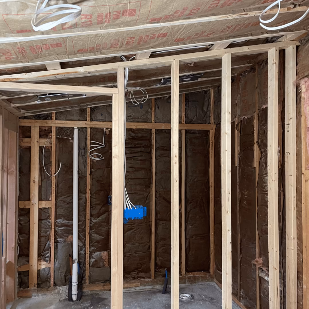 Open wall framing with insulation, wiring, and a plumbing stack