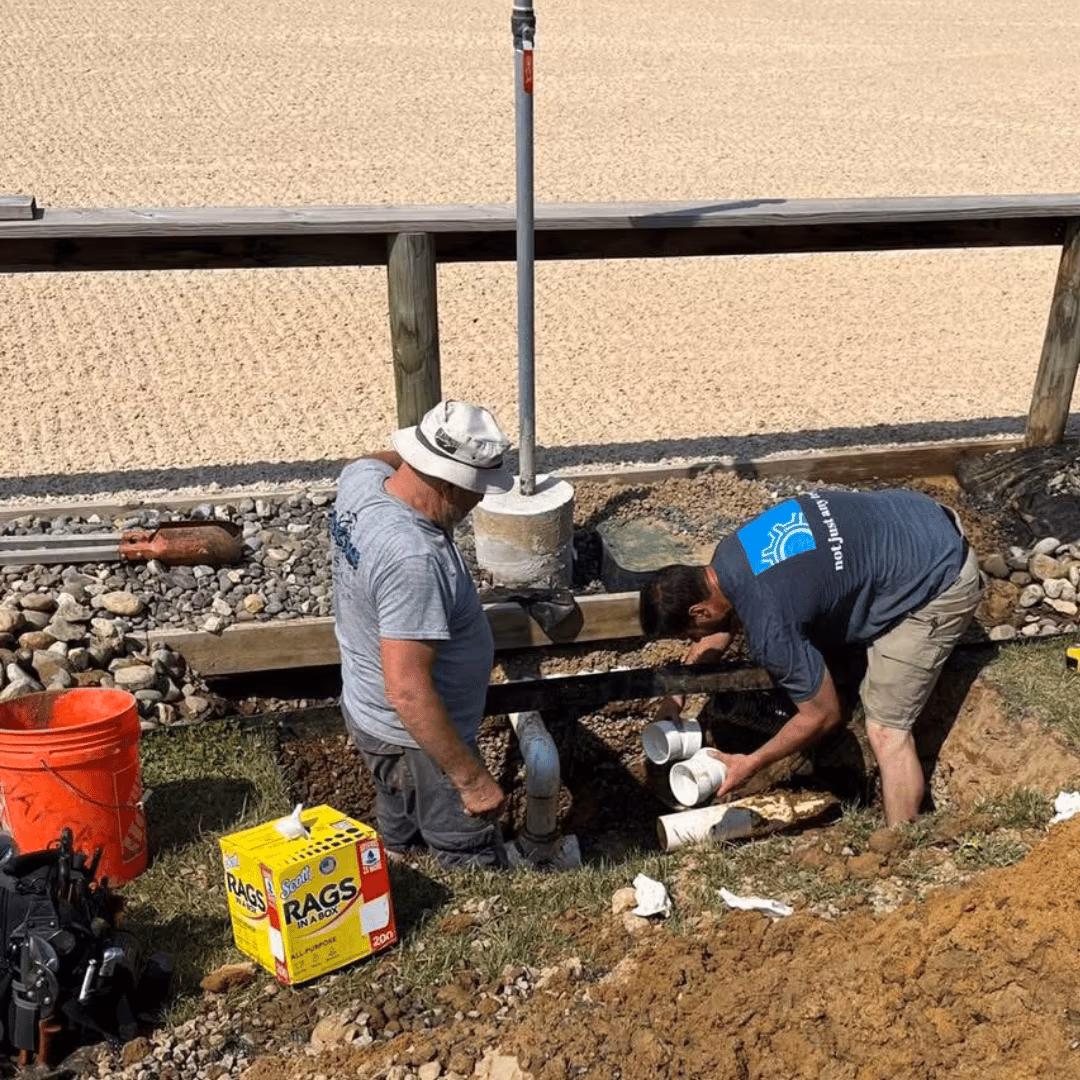 Two technicians repairing a sewer line in an excavated trench